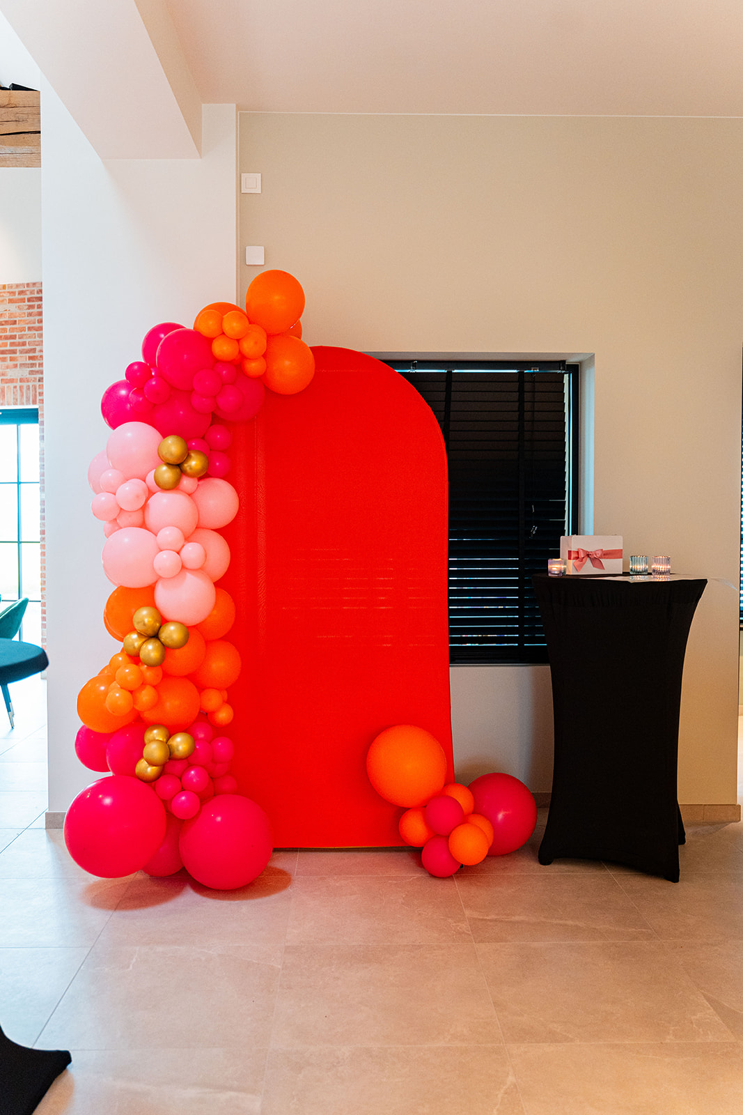 Kleurrijke ballonnenboog in roze, oranje en goud bij rode boog