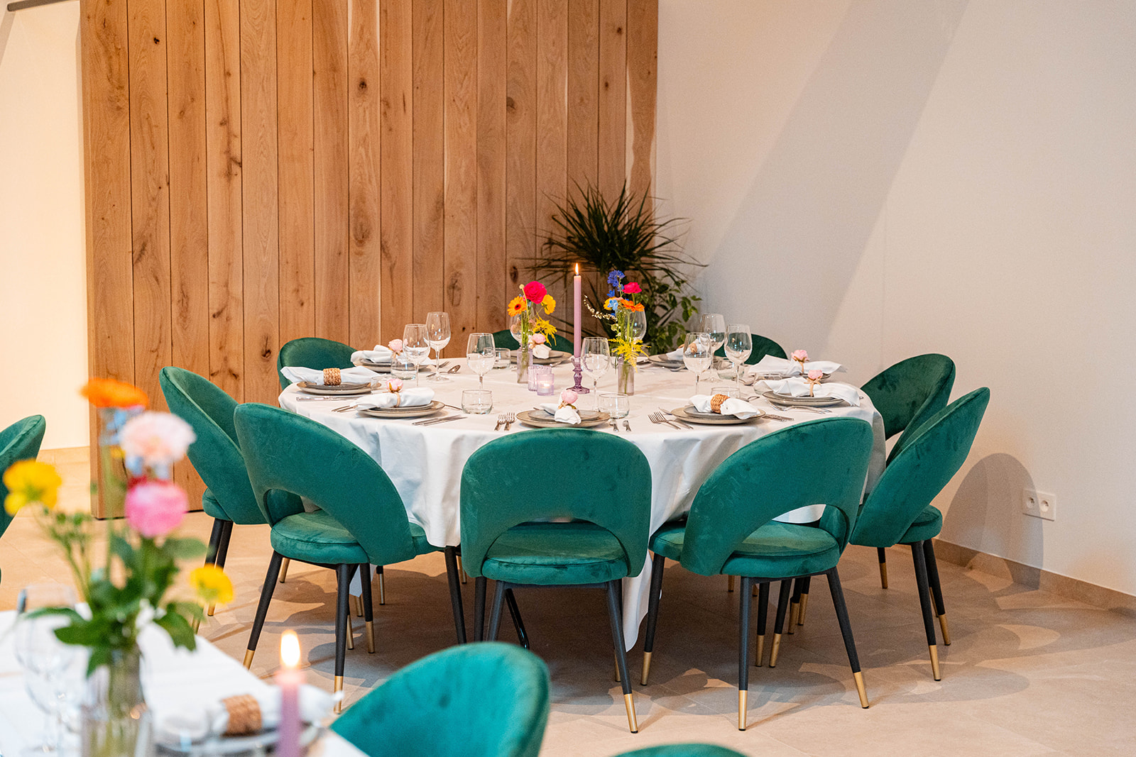 Ronde feesttafel met smaragdgroene velvet stoelen tegen houten wand