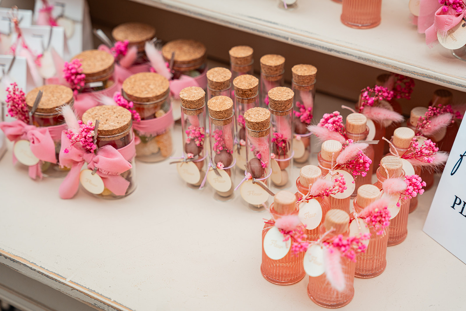 Bedankjes met roze bloemen en kurk in glazen flesjes op buffet