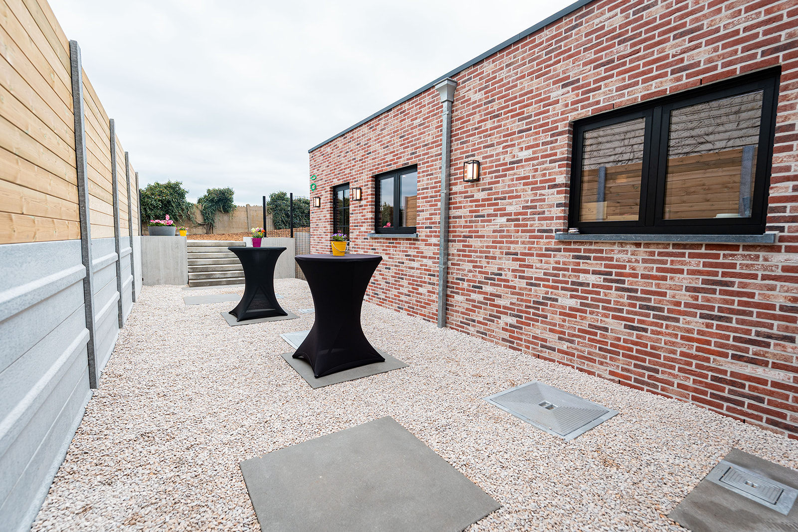 Sfeervol terras met statafels en bloemen langs de bakstenen gevel