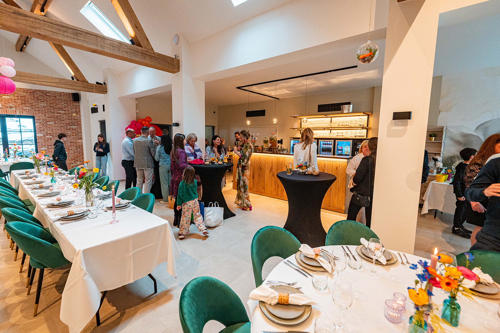 Sfeervolle feestzaal met houten balken, lange tafels, statafels en bar