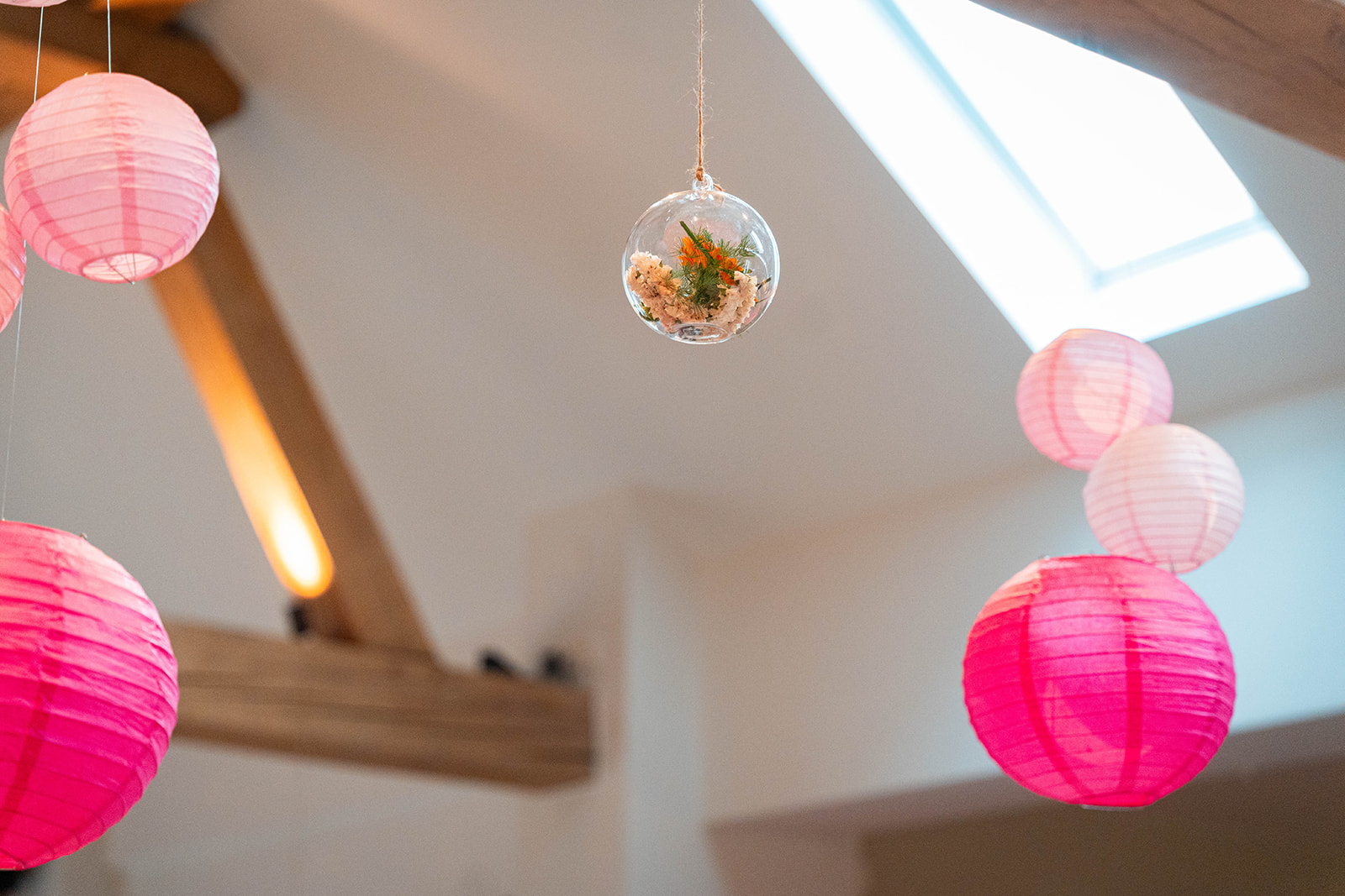 Sfeervolle decoratie met roze lampionnen en hangende bloemenbol onder houten balken