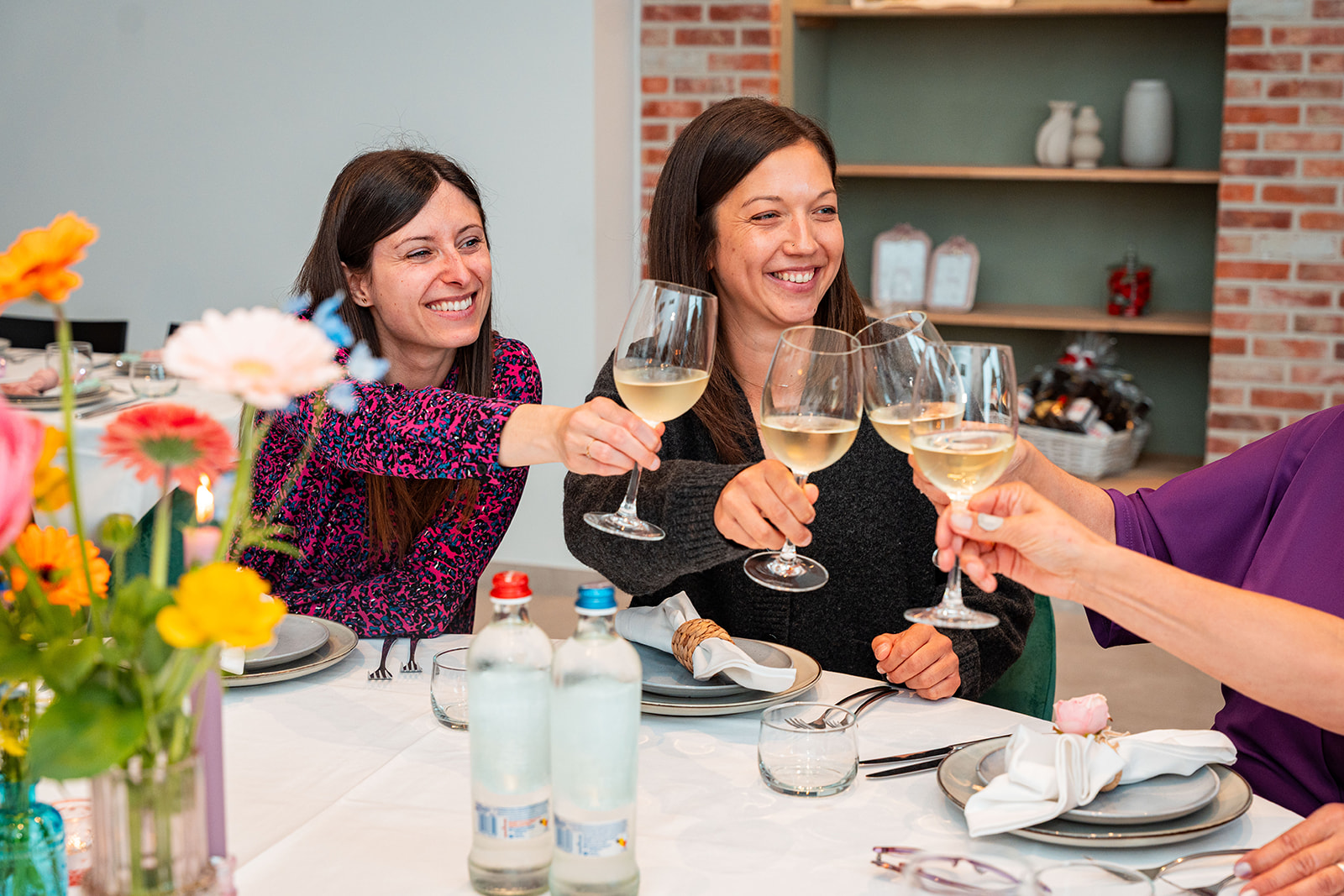 Lachende gasten klinken met witte wijn aan een gedekte feesttafel