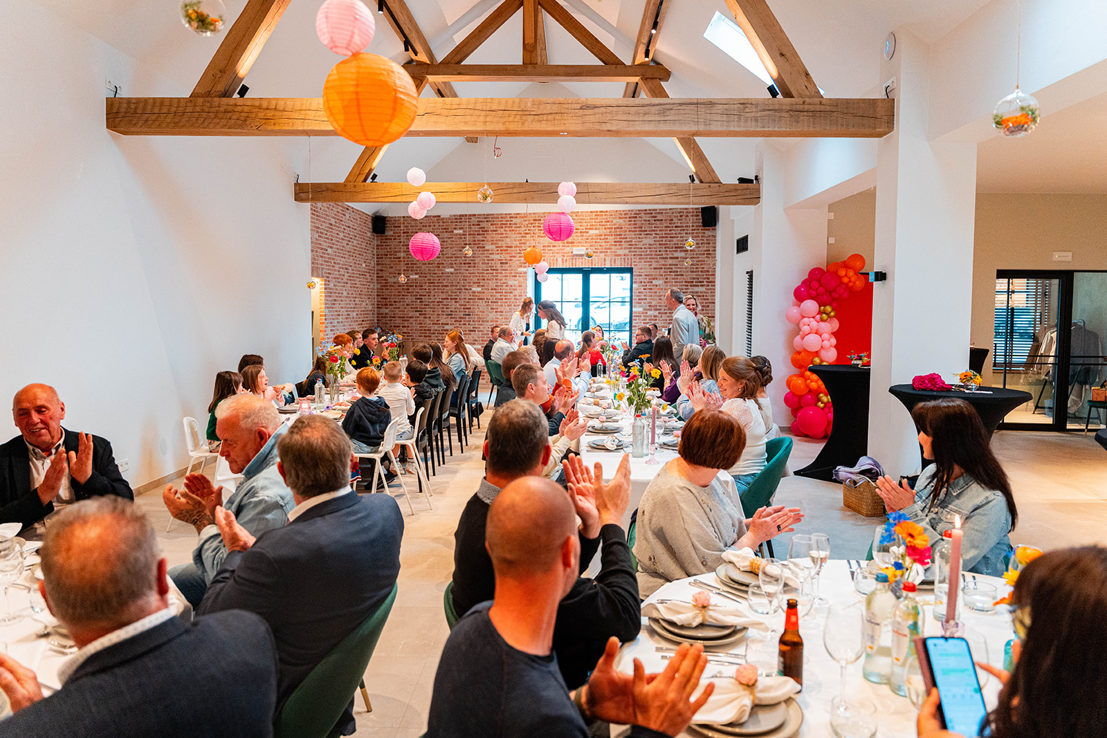 Volle feestzaal met klappende gasten, kleurrijke lampionnen en ballonnenboog
