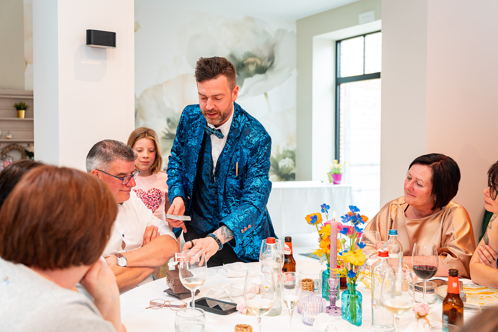 Goochelaar toont kaartentruc aan gasten rond gedekte ronde tafel met bloemen