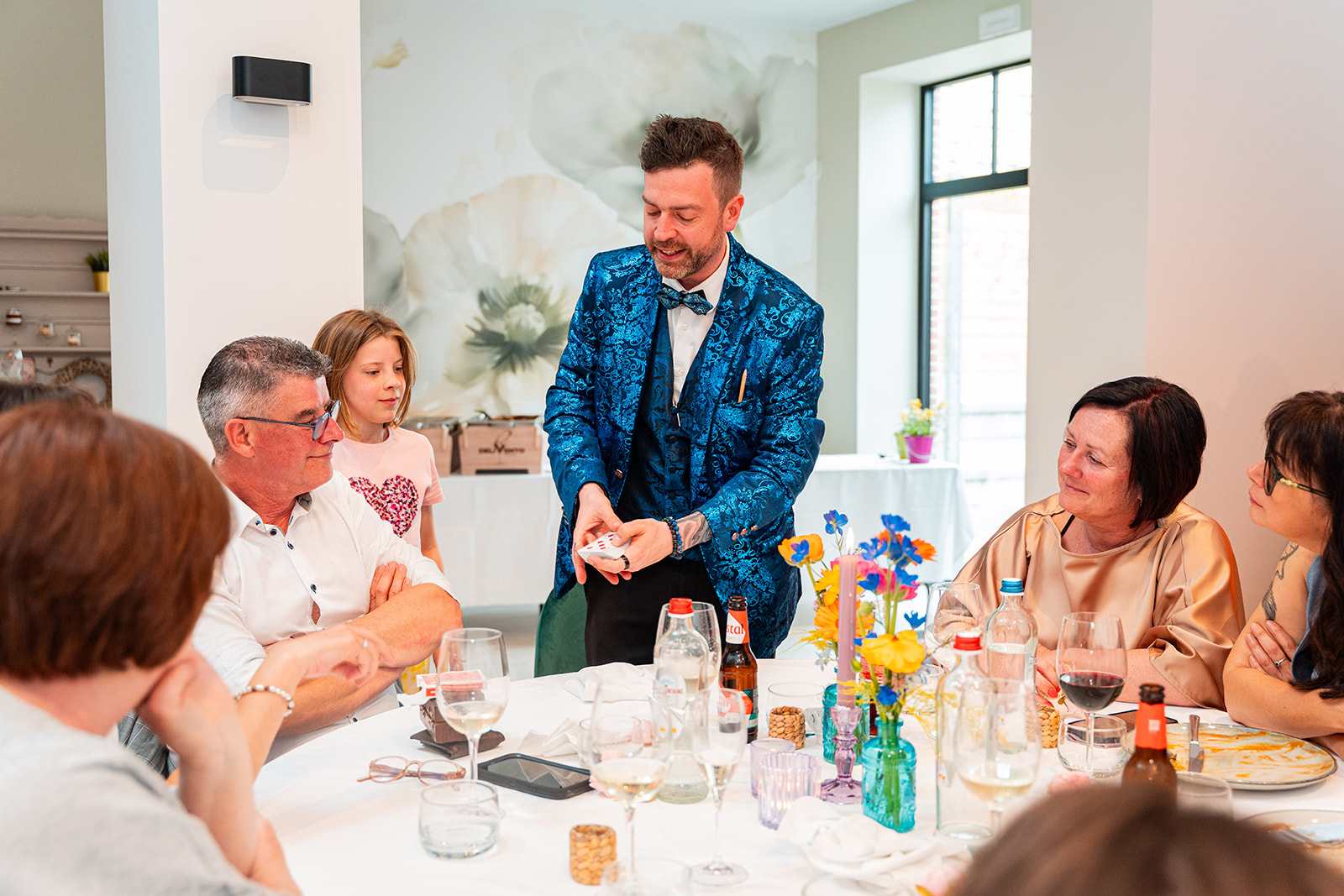 Goochelaar voert kaartentruc uit voor lachende gasten aan ronde feesttafel
