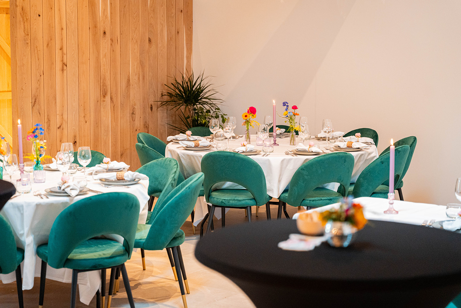 Ronde tafels met smaragdgroene velvet stoelen en kleurrijke bloemen