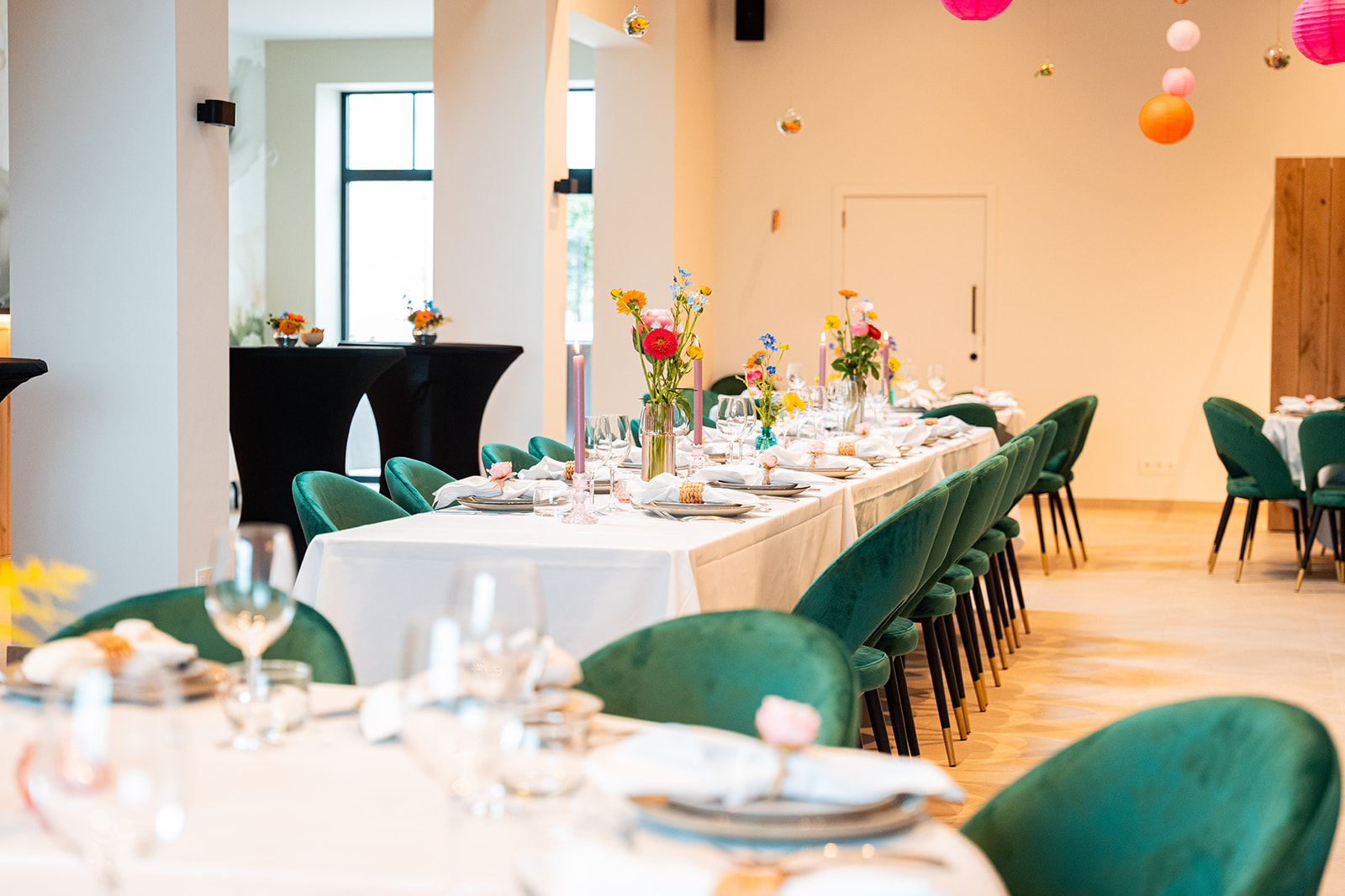 Lange feesttafel met smaragdgroene velvet stoelen en kleurrijke lampionnen