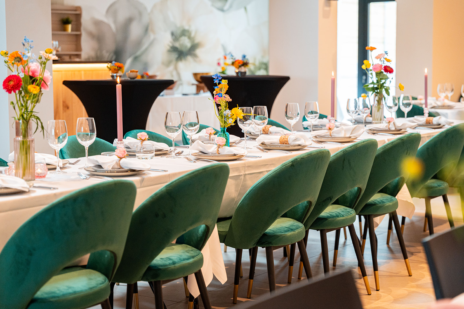 Detail van feesttafel met smaragdgroene stoelen, glaswerk en bloemen